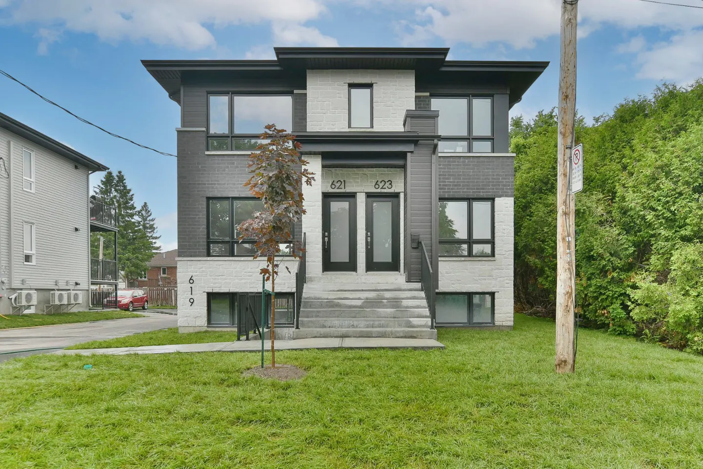 Modern duplex with gray brick and white stone facade, black trim, and two black front doors with addresses 621 and 623. Green lawn.