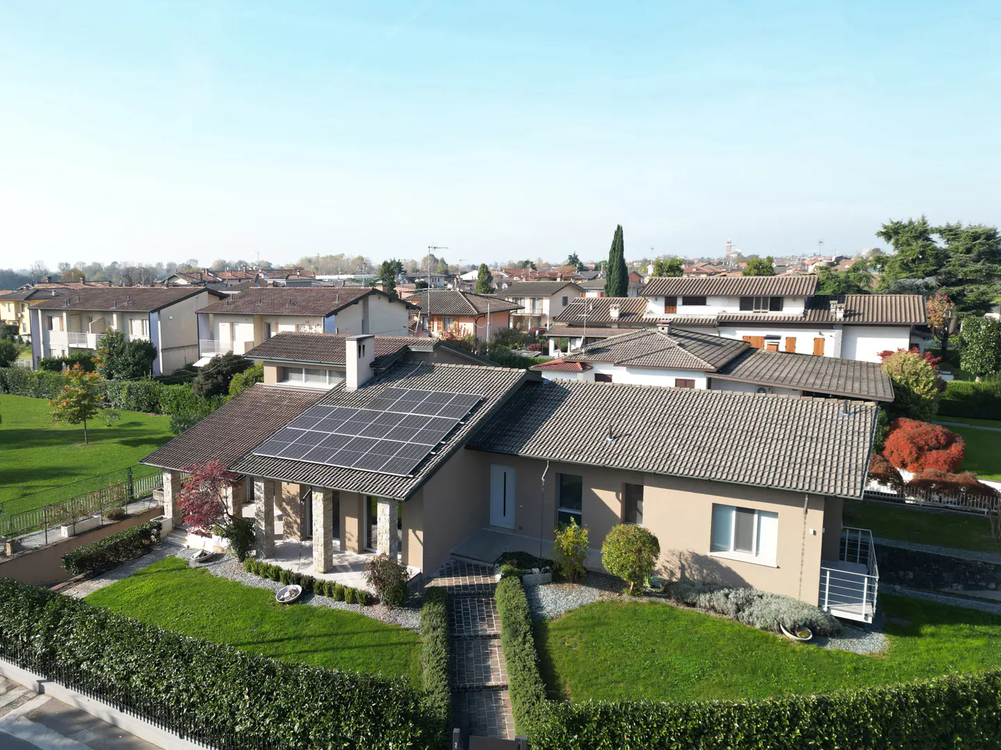 Aerial view of a beige single-story home with solar panels, green lawn, and trimmed hedges in a residential neighborhood.