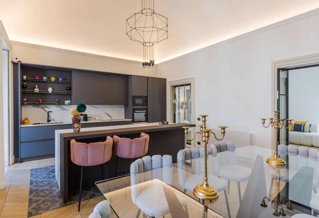 A modern kitchen and dining area with gray cabinets, pink bar stools, and a glass table with gold candelabras.