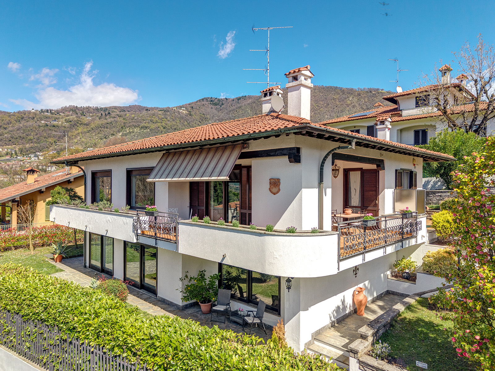 Exterior view of a two-story white house with a red tile roof and wrought iron balconies. Mountains and blue sky in the background. [AI-generated text]