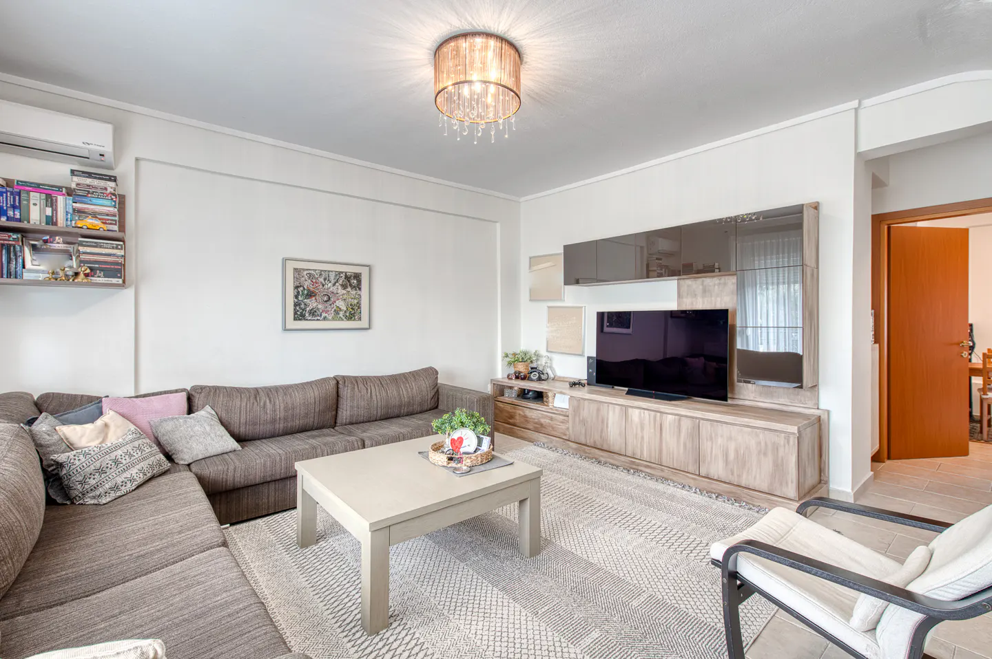 Living room with a brown sectional sofa, a light gray coffee table, and a large TV on a wooden console. A patterned rug covers the floor.
