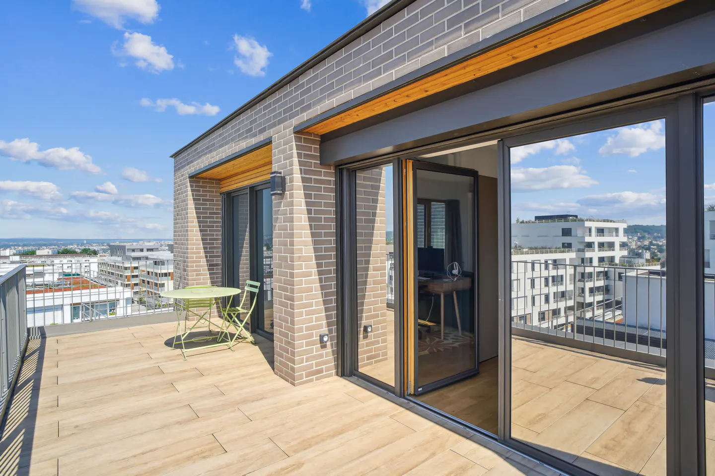 A modern rooftop patio with a green table and chairs, brick walls, and sliding glass doors.