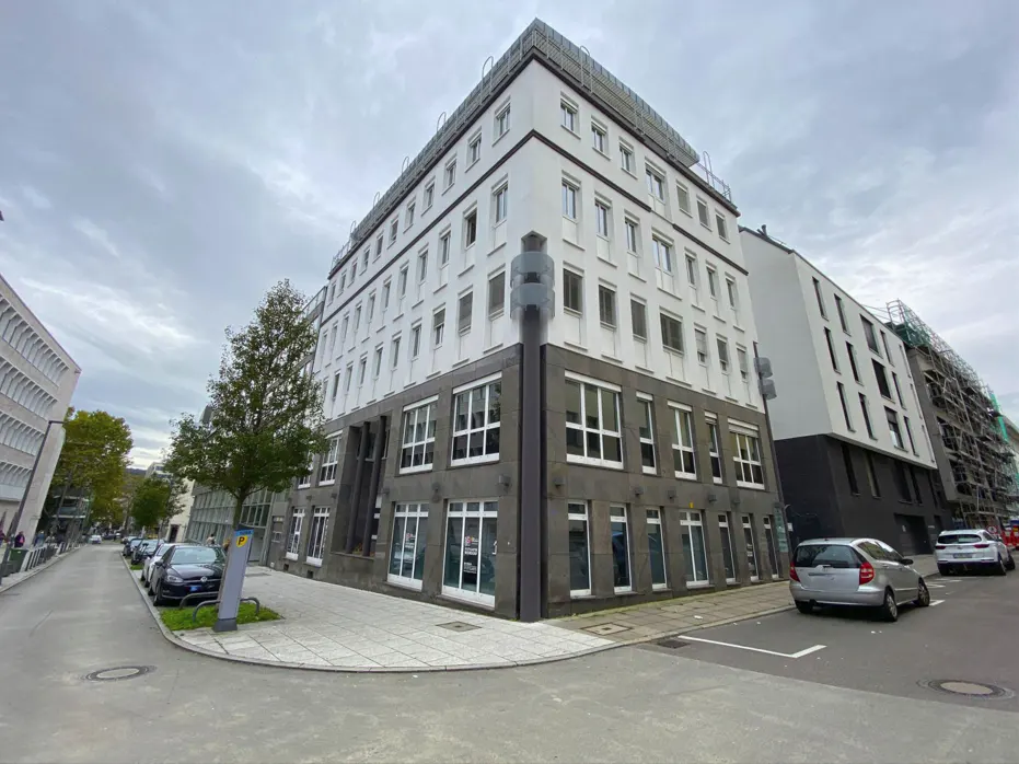 Corner view of a modern multi-story building with a white upper facade and dark stone ground floor on a city street.
