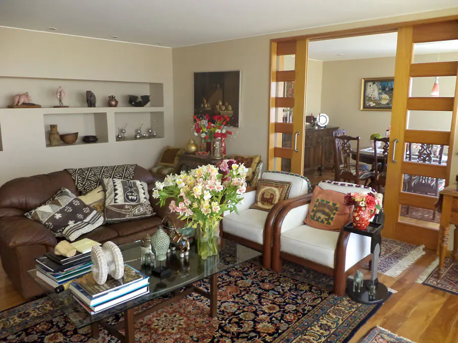 Living room with brown leather sofa, white armchairs, glass coffee table, and sliding wood doors to dining room.