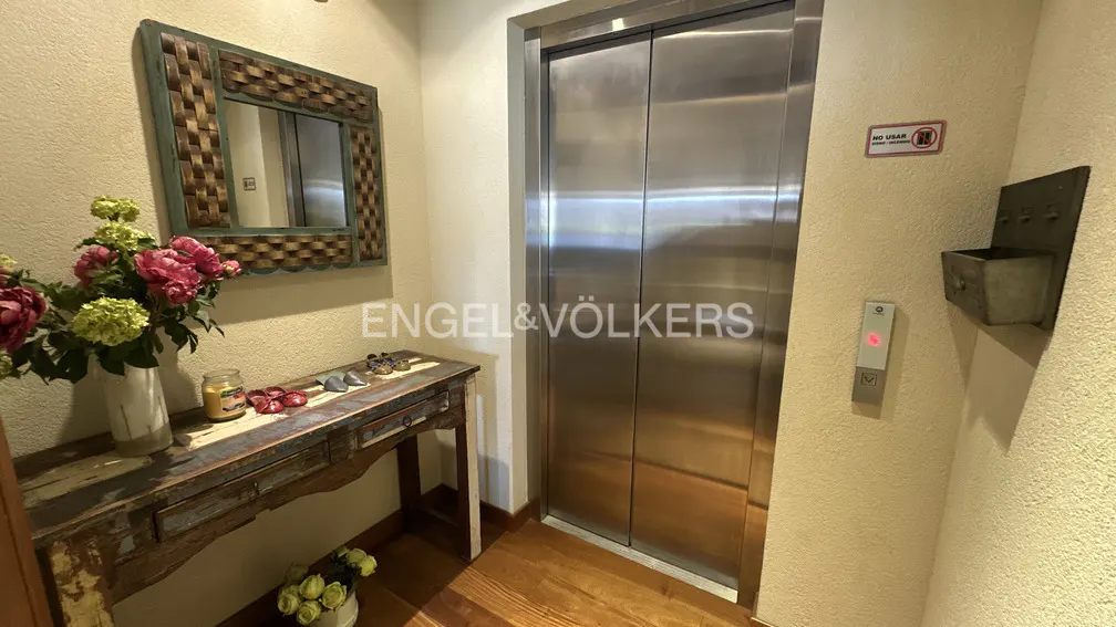 Hallway with a stainless steel elevator, a rustic wooden table with flowers, and a decorative mirror.