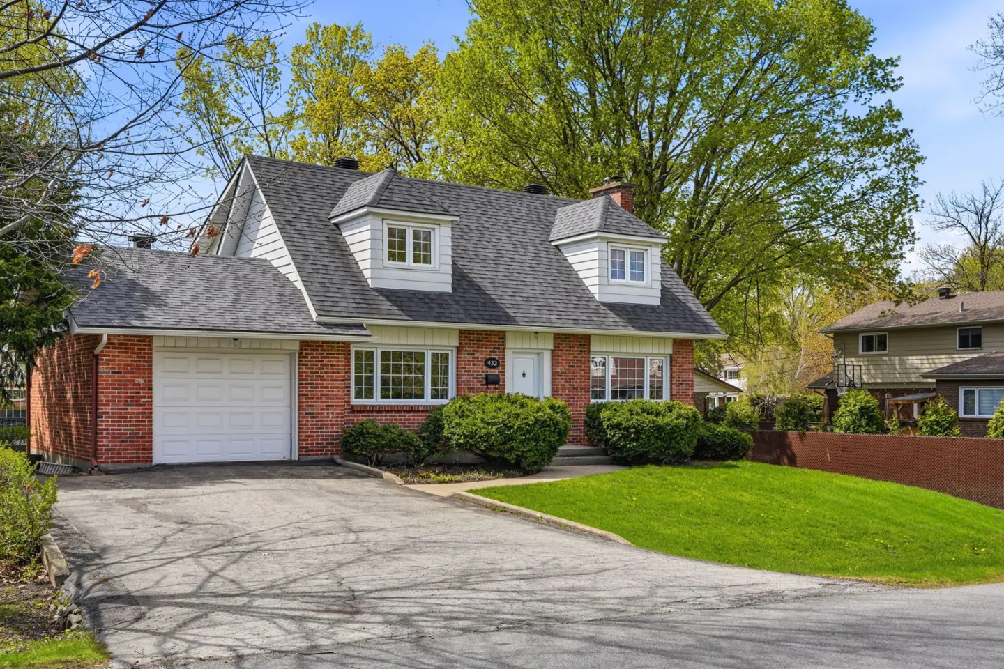 Red brick house with a gray roof, white garage door, and green lawn on a sunny day.