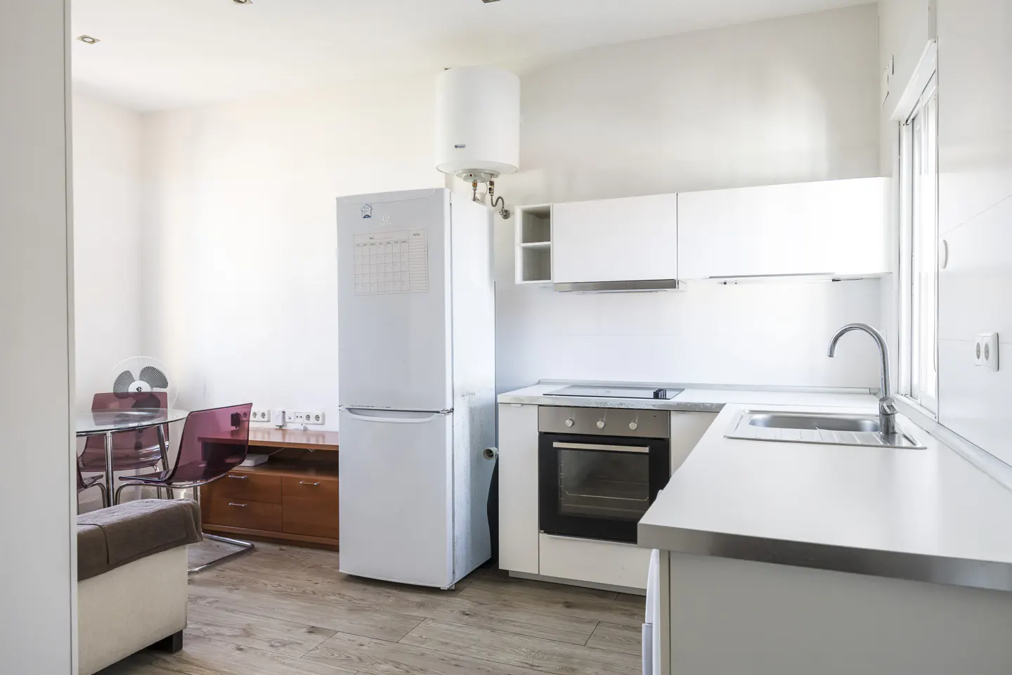 Bright, modern kitchen with white cabinets, stainless steel sink, and appliances. A dining table with red chairs is visible in the background.