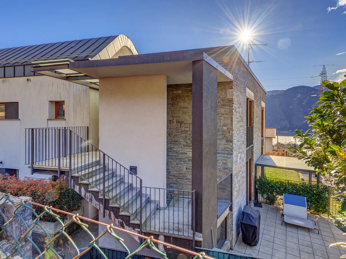 Exterior view of a modern two-story house with stone and stucco walls, a metal roof, and a patio with a grill.