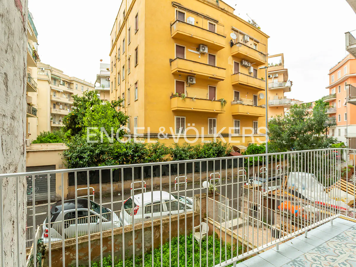 View from a balcony with white railings overlooking a street with parked cars and yellow buildings in the background.