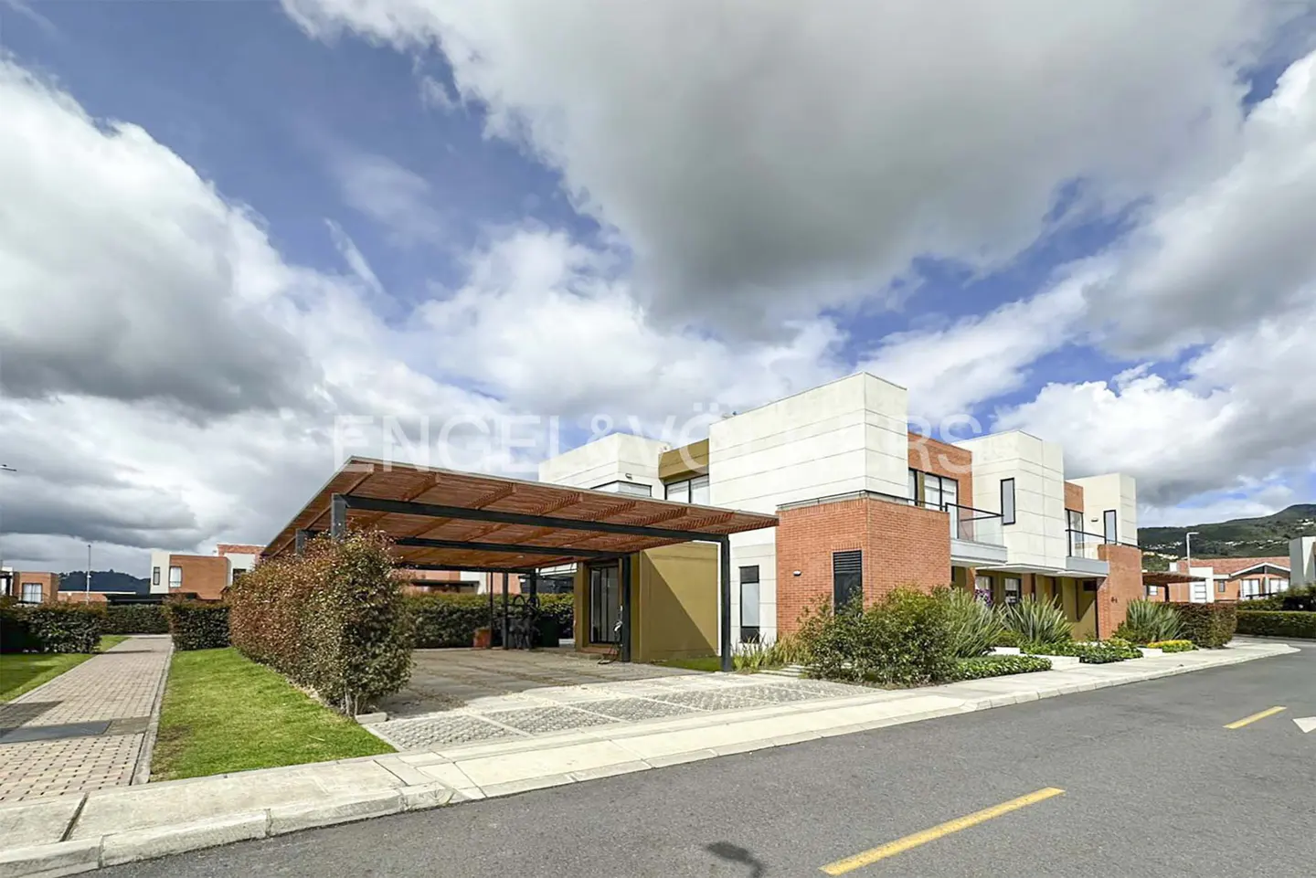 Modern townhouses with brick and white facades, covered parking, and manicured landscaping under a cloudy sky.