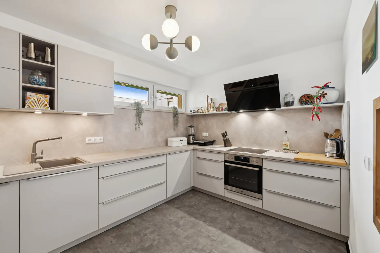 Bright kitchen with gray cabinets, gray countertops, and gray floor. A modern light fixture hangs from the ceiling. Appliances are visible.