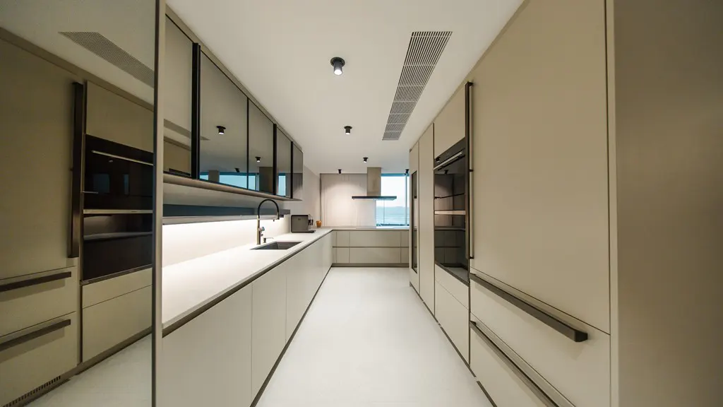 A modern kitchen with beige cabinets, black-framed glass doors, and a white countertop. A sink and faucet are visible. The floor is white.