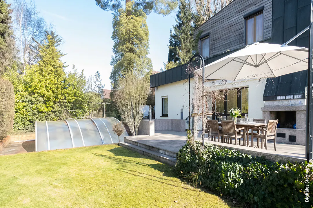 A backyard with a pool cover, green grass, a patio with a table and chairs, and a fireplace.