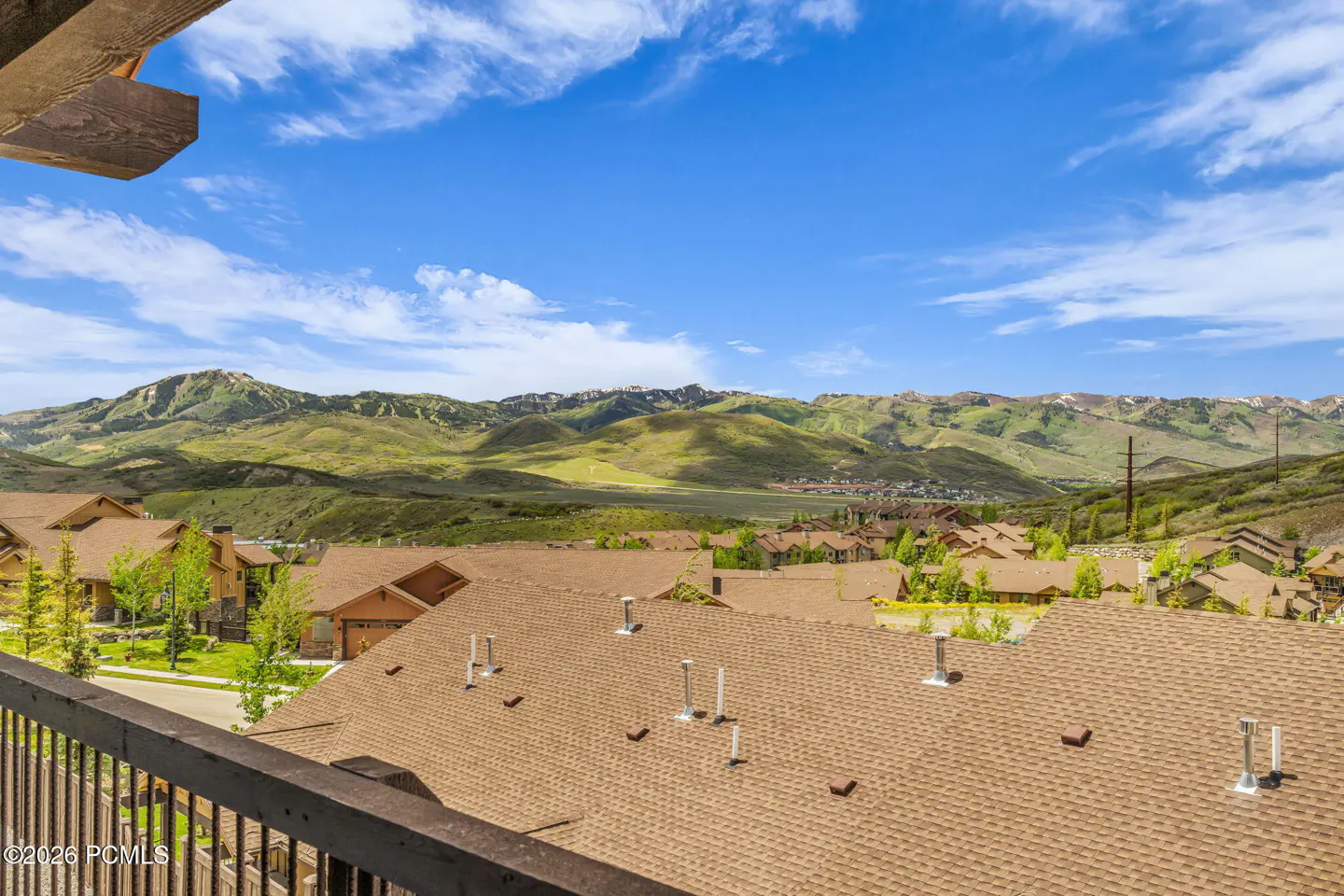 View from a balcony overlooking a neighborhood of brown-roofed homes with a scenic mountain range under a blue sky.