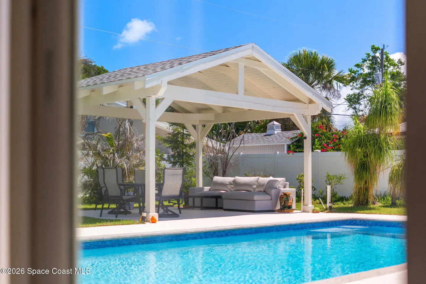 A backyard with a pool and a white pergola with outdoor furniture.