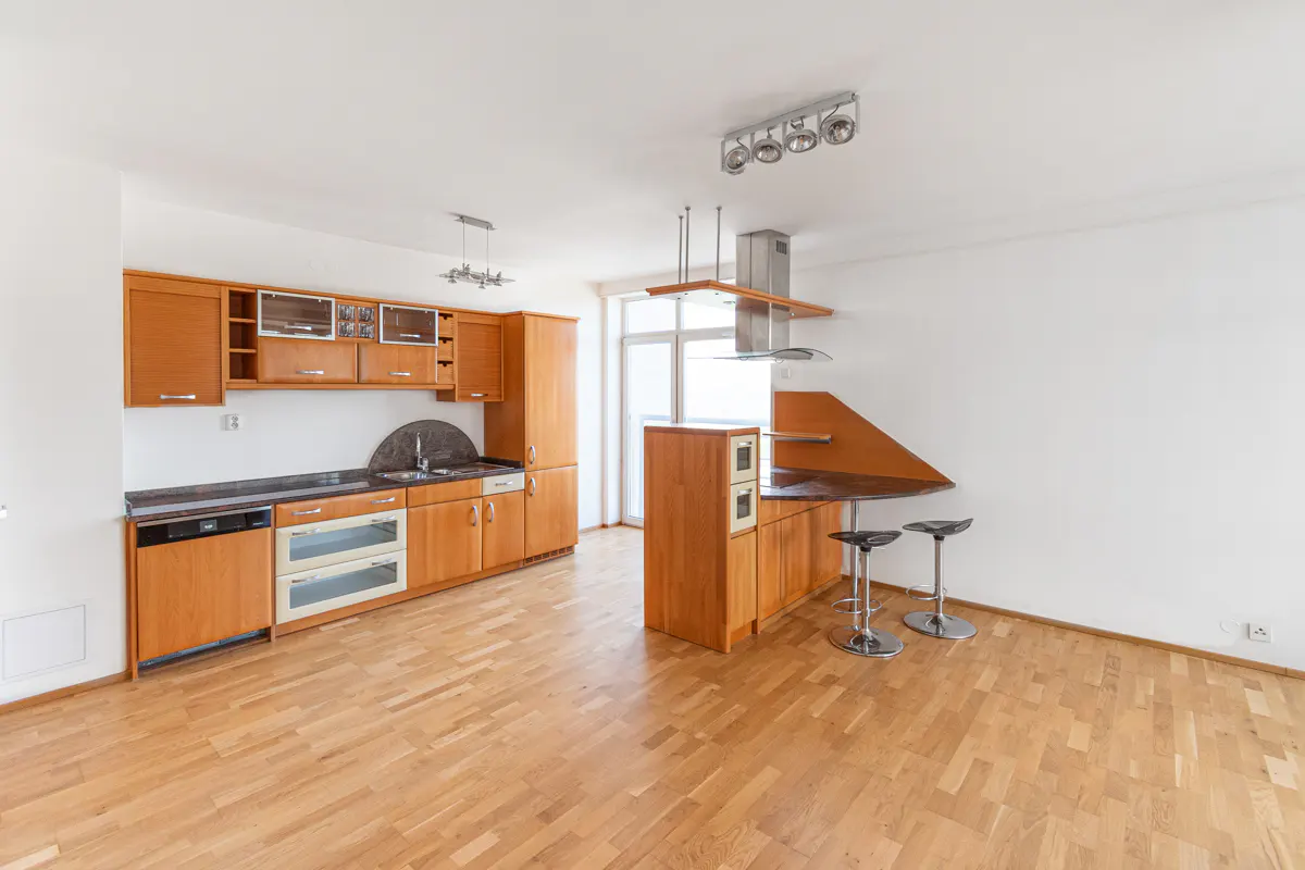 Bright kitchen with wood cabinets, stainless steel appliances, and a breakfast bar with two stools on a light wood floor.