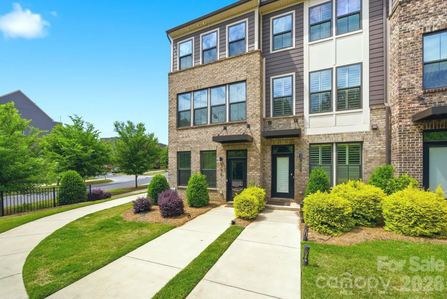 Exterior of a three-story brick townhouse with a concrete driveway and green lawn.