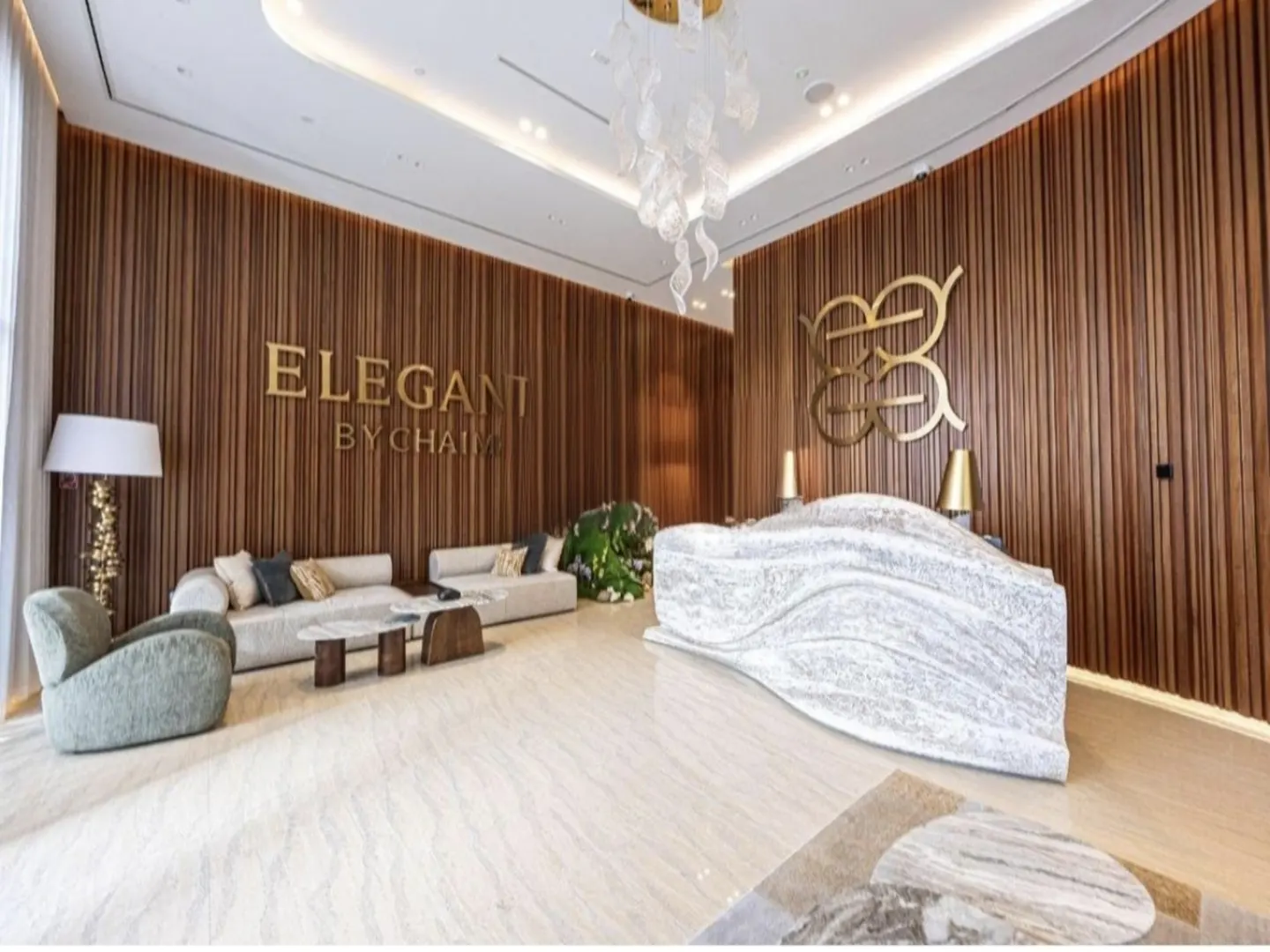 Modern office lobby with wood-paneled walls, a white marble reception desk, lounge seating, and a decorative chandelier.