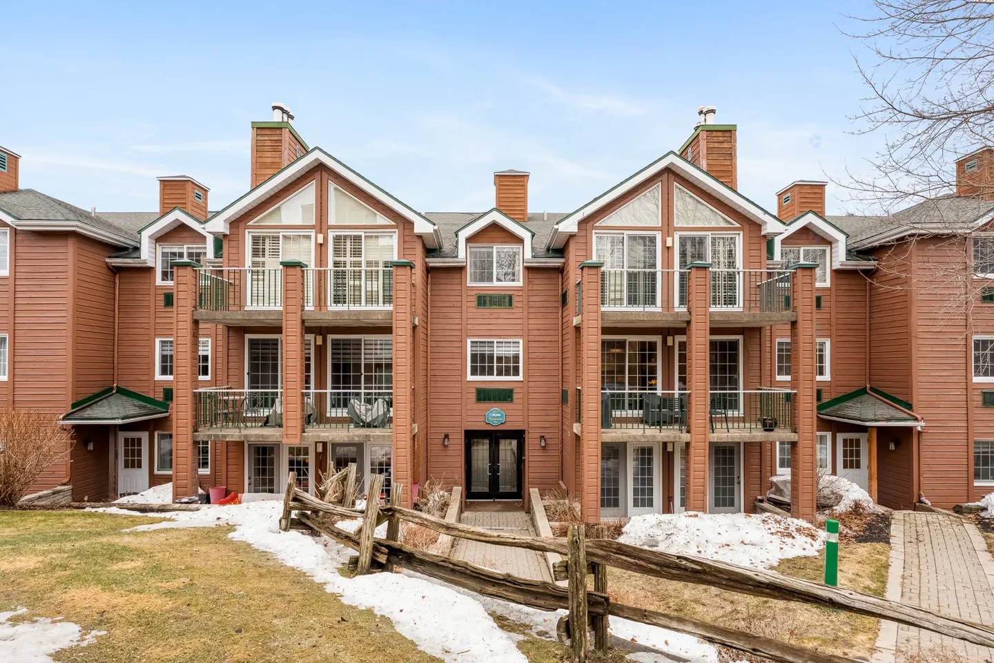 Exterior of a brown condo building with balconies and a wooden fence in front.