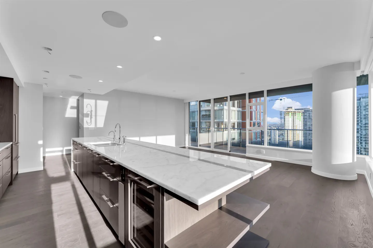 Bright, modern kitchen with a large island, marble countertop, and city views through floor-to-ceiling windows.