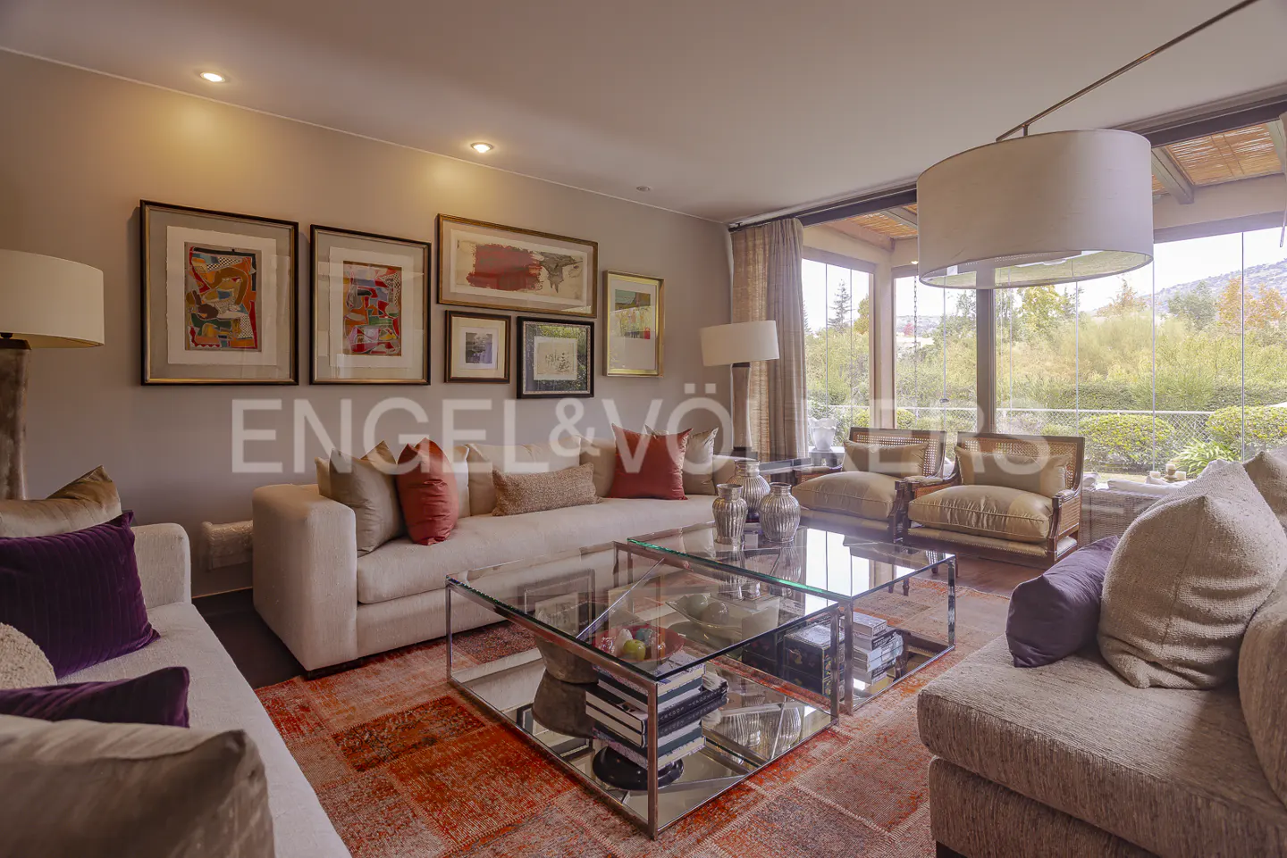 Living room with sofas, glass coffee table, and art on the wall. Large windows overlook a green landscape.