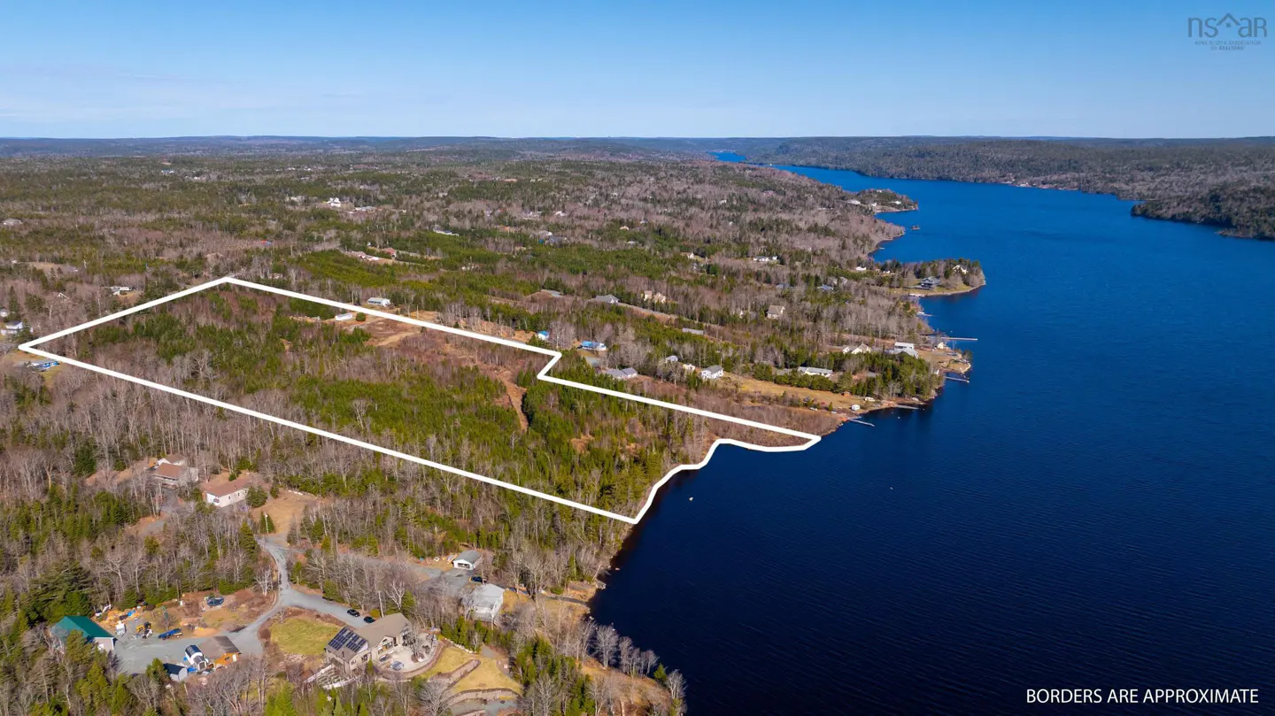 Aerial view of a wooded lot outlined in white, bordering a blue lake under a clear sky.