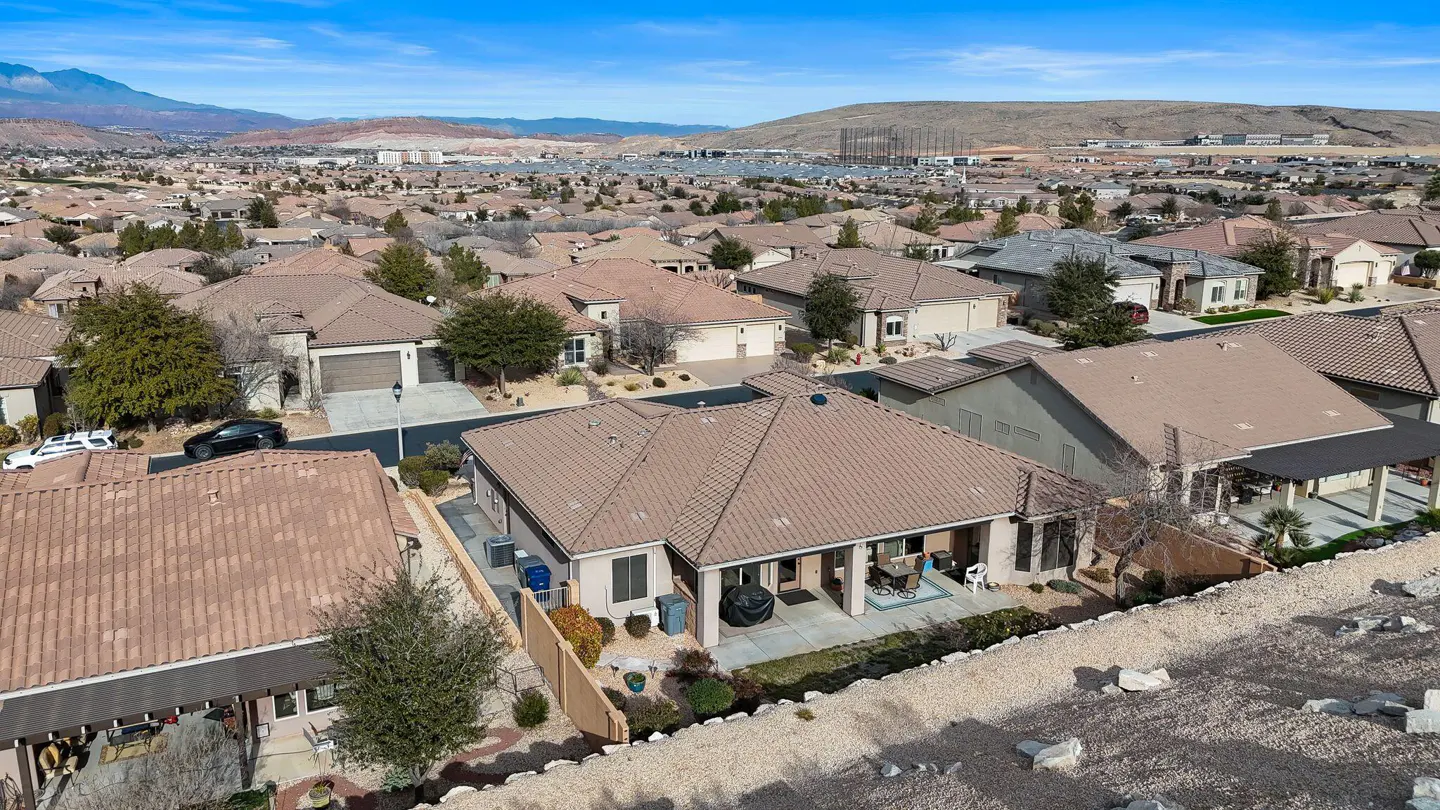Aerial view of a beige single-family home with a brown tile roof in a suburban neighborhood under a blue sky.