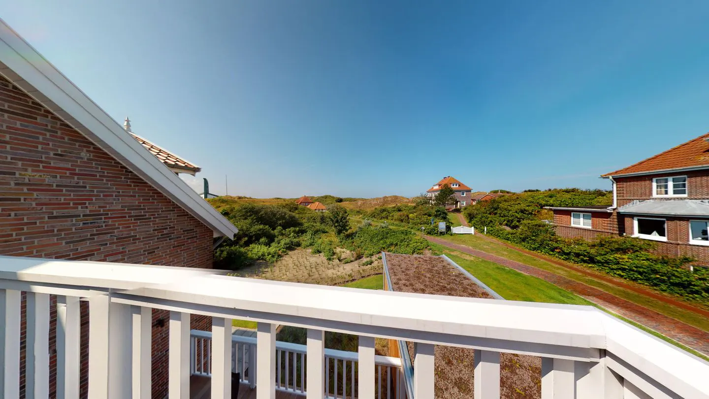 View from a white balcony overlooking houses with red roofs, green grass, and a clear blue sky.