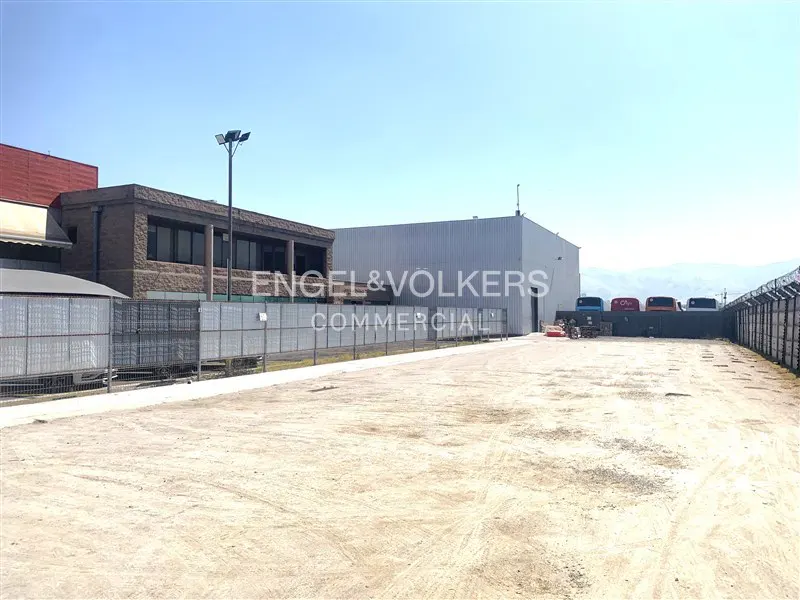 Commercial property with a large dirt lot, buildings, and a fence under a clear blue sky.