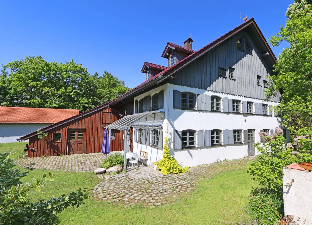 Exterior view of a two-story white house with gray shutters and a red roof, surrounded by green grass and trees.