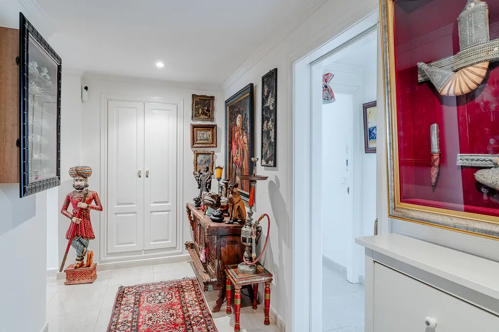Hallway with white walls, a red rug, and various decorations, including a wooden statue and framed art.