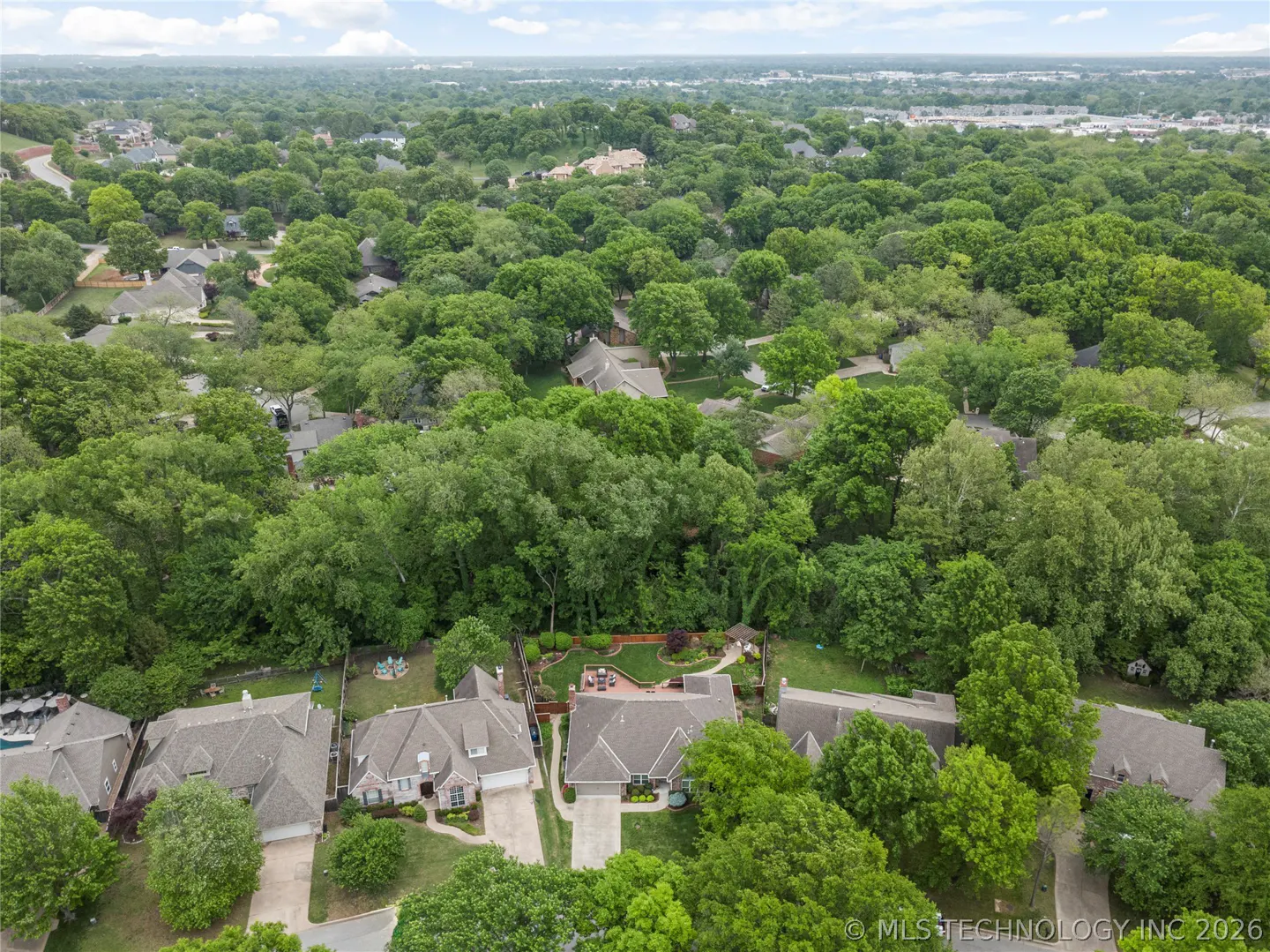 Aerial view of a neighborhood with houses surrounded by lush green trees under a cloudy sky.