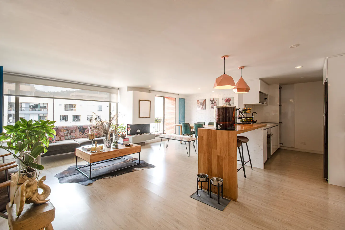 Bright, open-concept living space with wood floors, a modern kitchen, and a large window overlooking a city view.