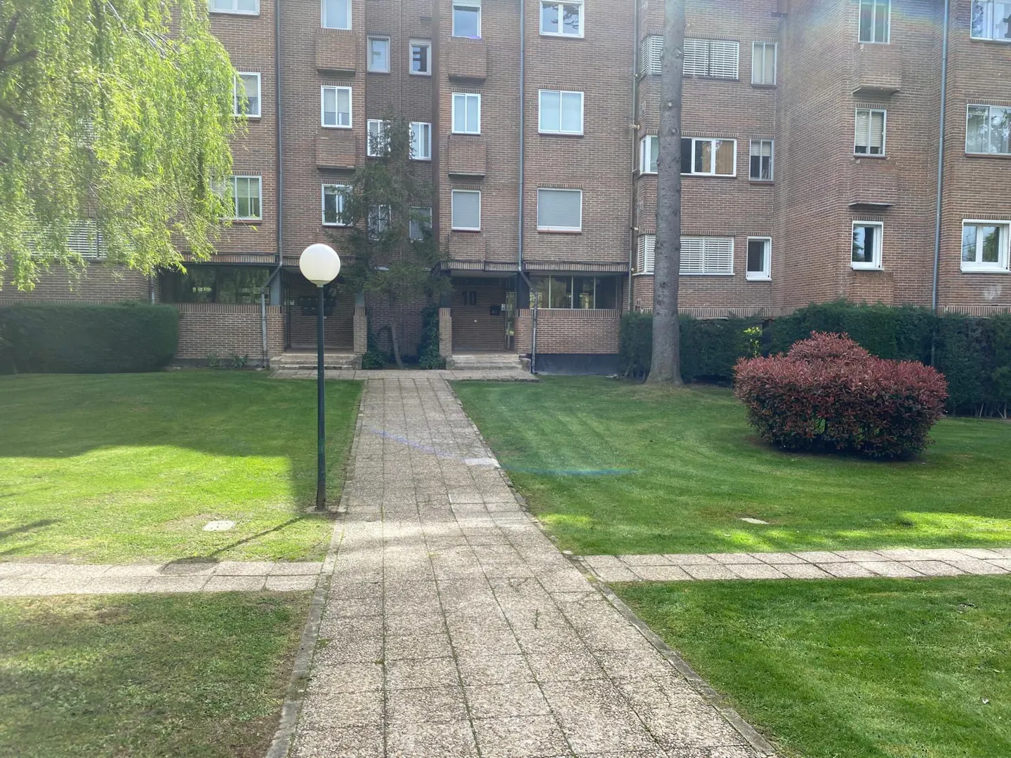 Brick apartment building with a stone walkway leading to the entrance, surrounded by green grass and landscaping.