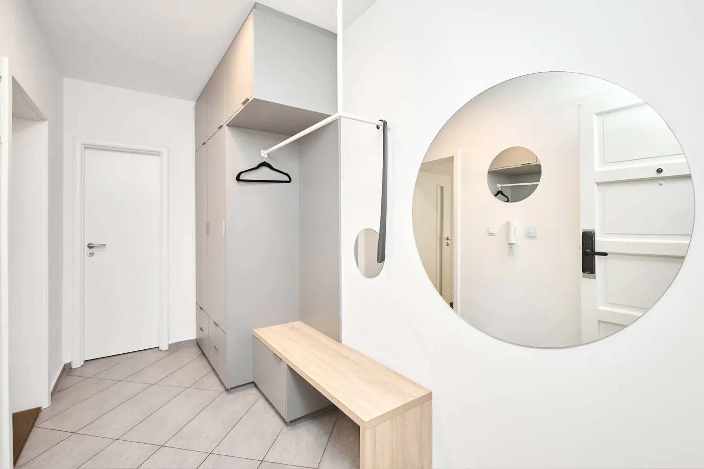 Bright entryway with gray storage, a light wood bench, and a round mirror reflecting a white door.
