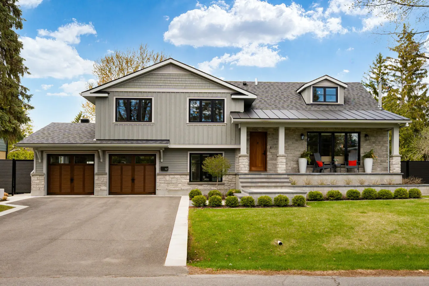 Two-story house with gray siding, stone accents, and a two-car garage. A green lawn and blue sky complete the scene.
