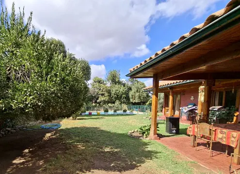 A view of a house with a red tile roof and a green lawn with trees under a blue sky with white clouds.