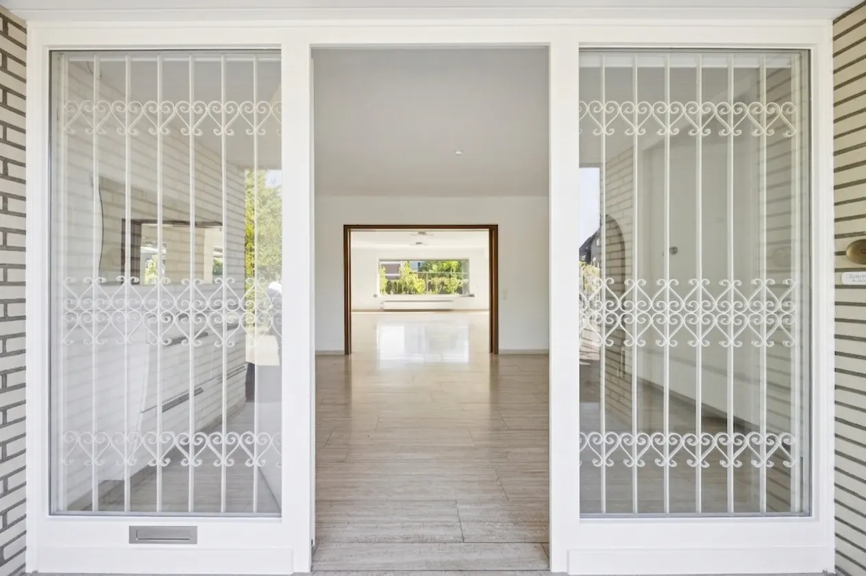Open white security gate reveals a bright, empty home interior with light wood floors and a view to the backyard.