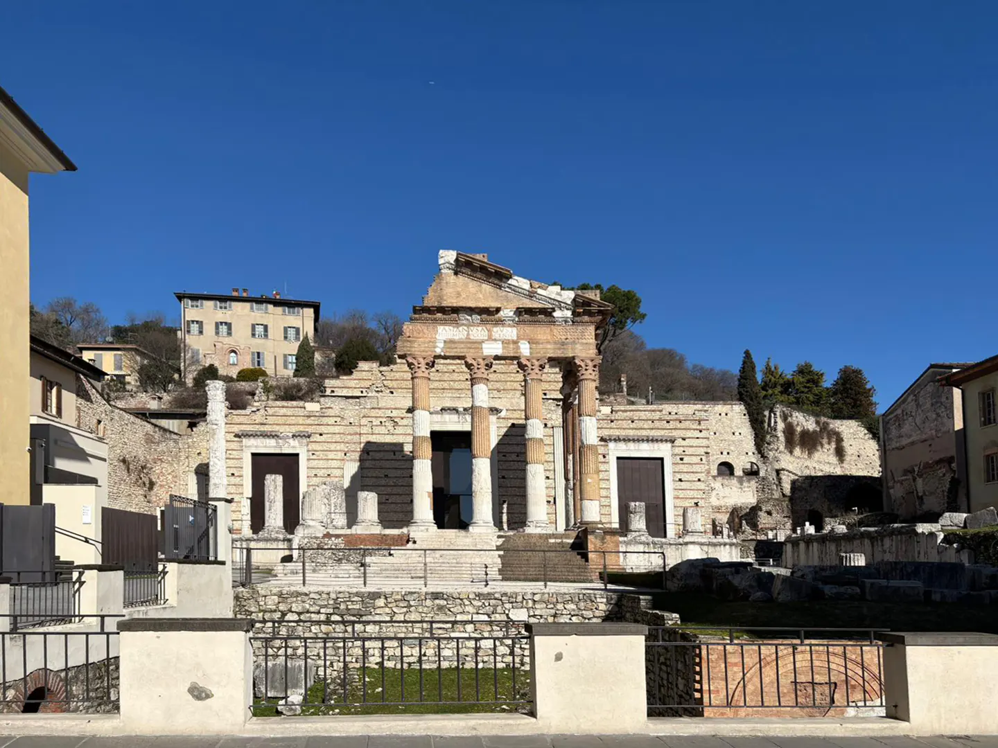 Ancient Roman temple ruins with columns and stone walls under a clear blue sky in Brescia, Italy.
