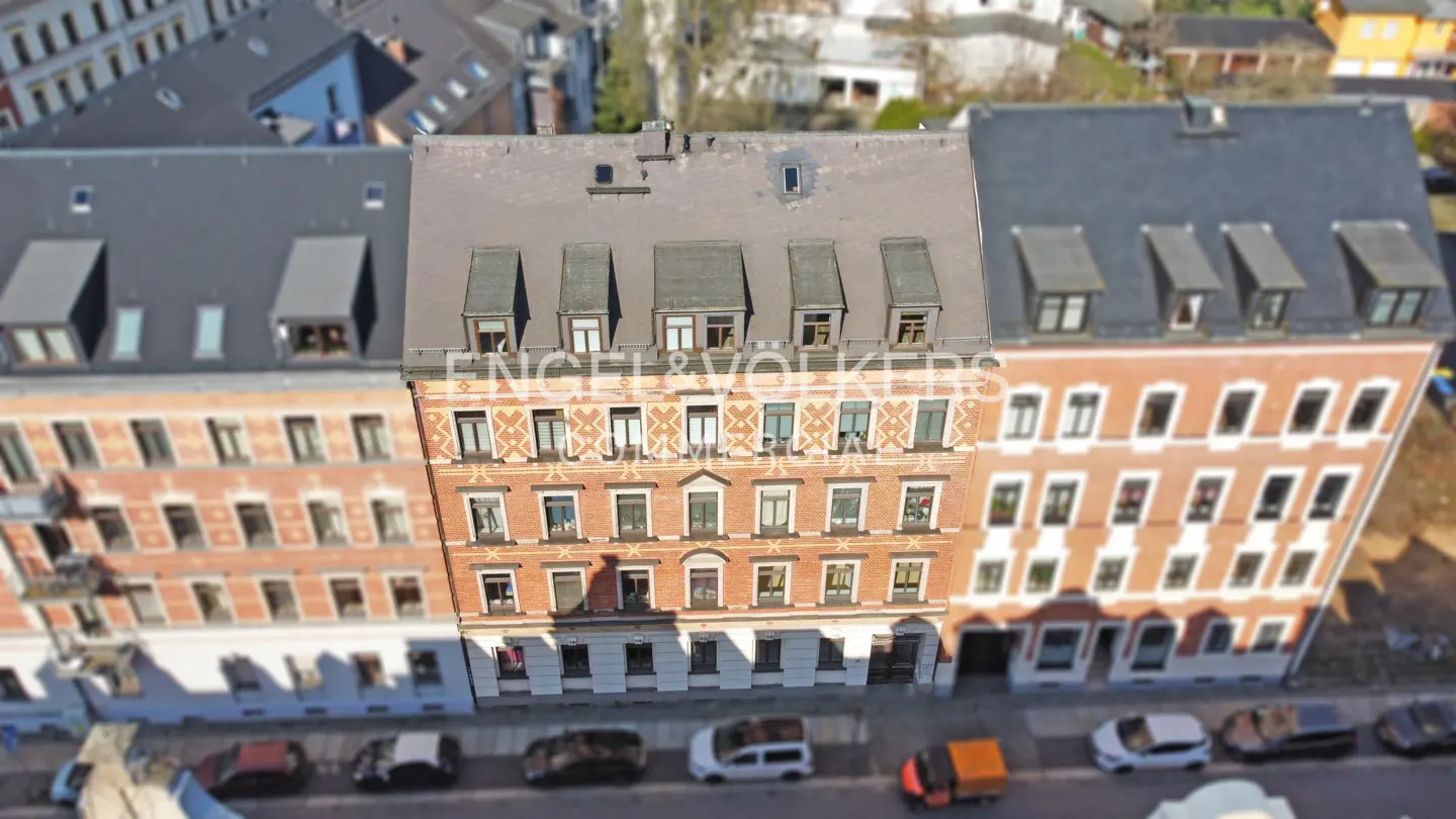 Aerial view of a red brick apartment building with dark gray roof, surrounded by similar buildings and parked cars.