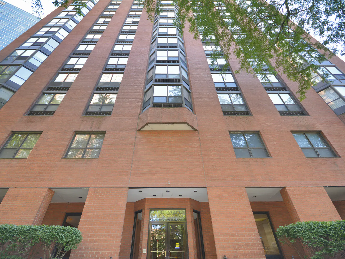 Exterior view of a tall brick apartment building with many windows and a glass door entrance.