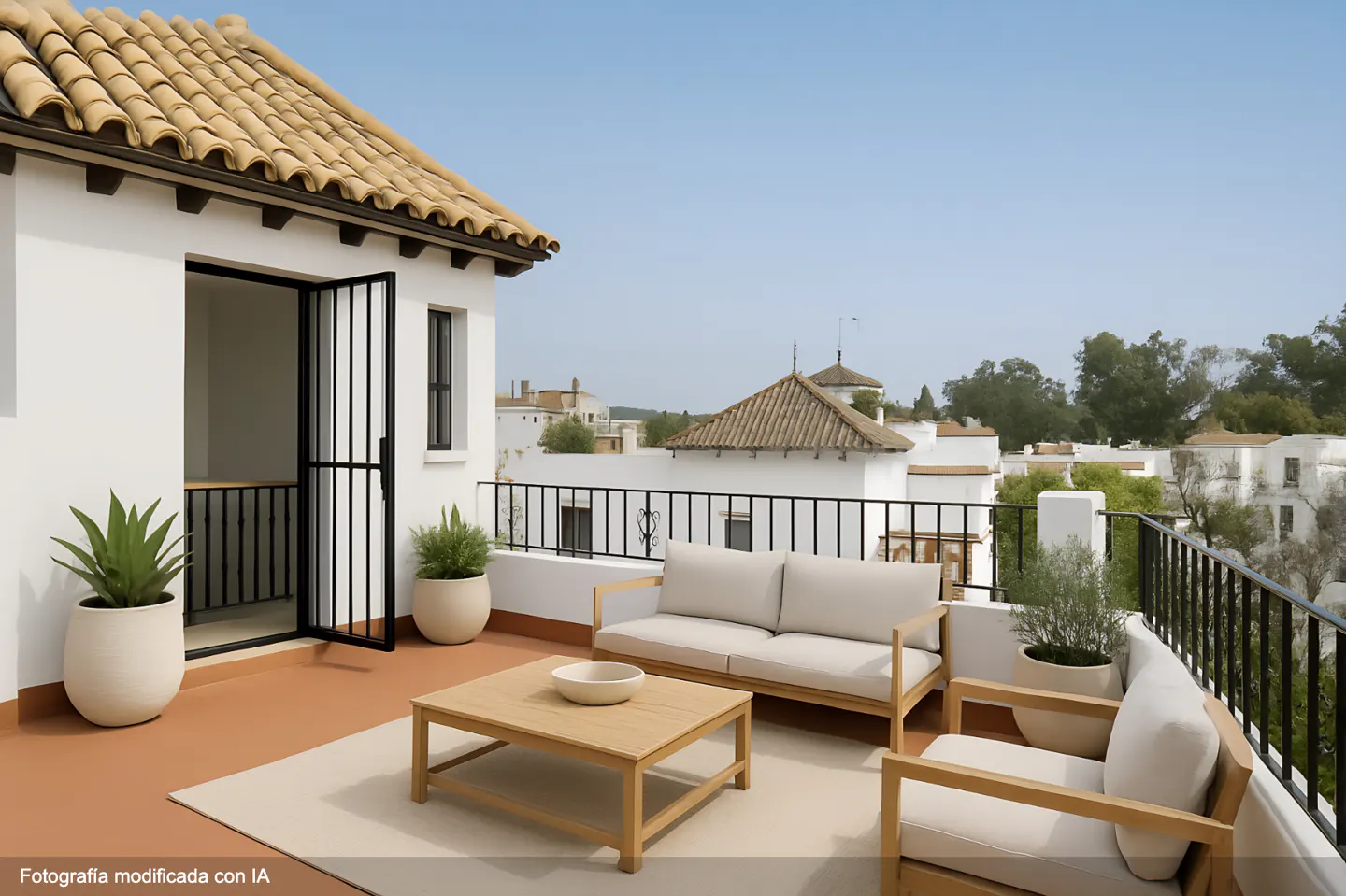 Rooftop patio with white walls, terracotta tile floor, and tan furniture. Balcony overlooks white buildings with terracotta roofs.