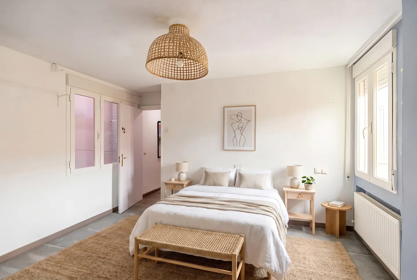 Bright bedroom with white walls, a bed with white linens, and a woven bench. A woven light fixture hangs from the ceiling.