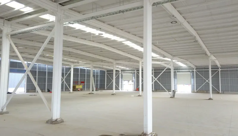 Interior of a large, empty warehouse with white steel beams and a concrete floor.