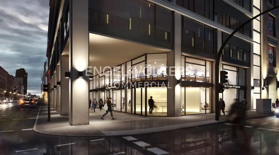 Exterior view of a modern commercial building with large glass windows and people walking by on the sidewalk at dusk.