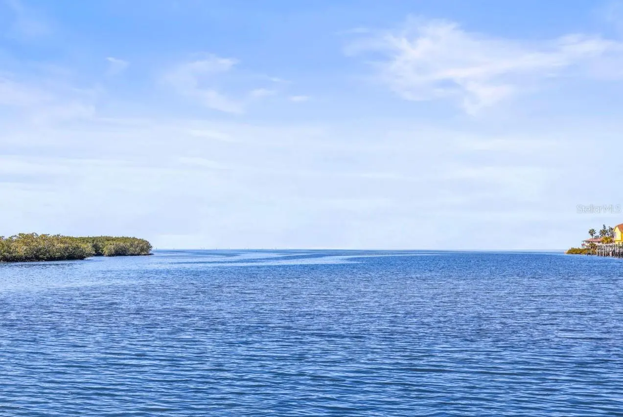 Calm blue water under a pale blue sky with wispy clouds. Green mangroves on the left, a house with a dock on the right.