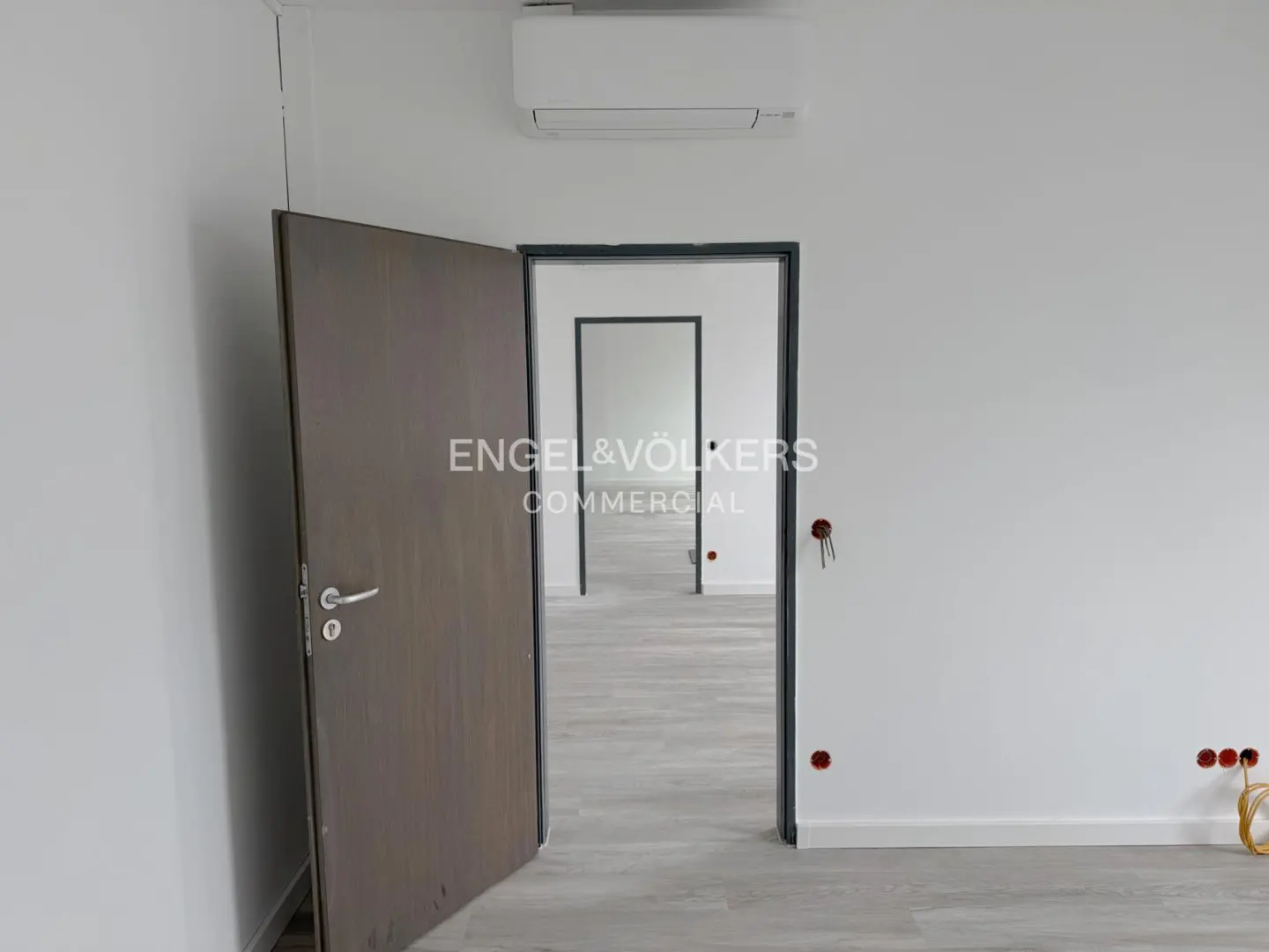 Interior view of a commercial space with white walls, grey wood floors, and open doorways leading to other rooms.
