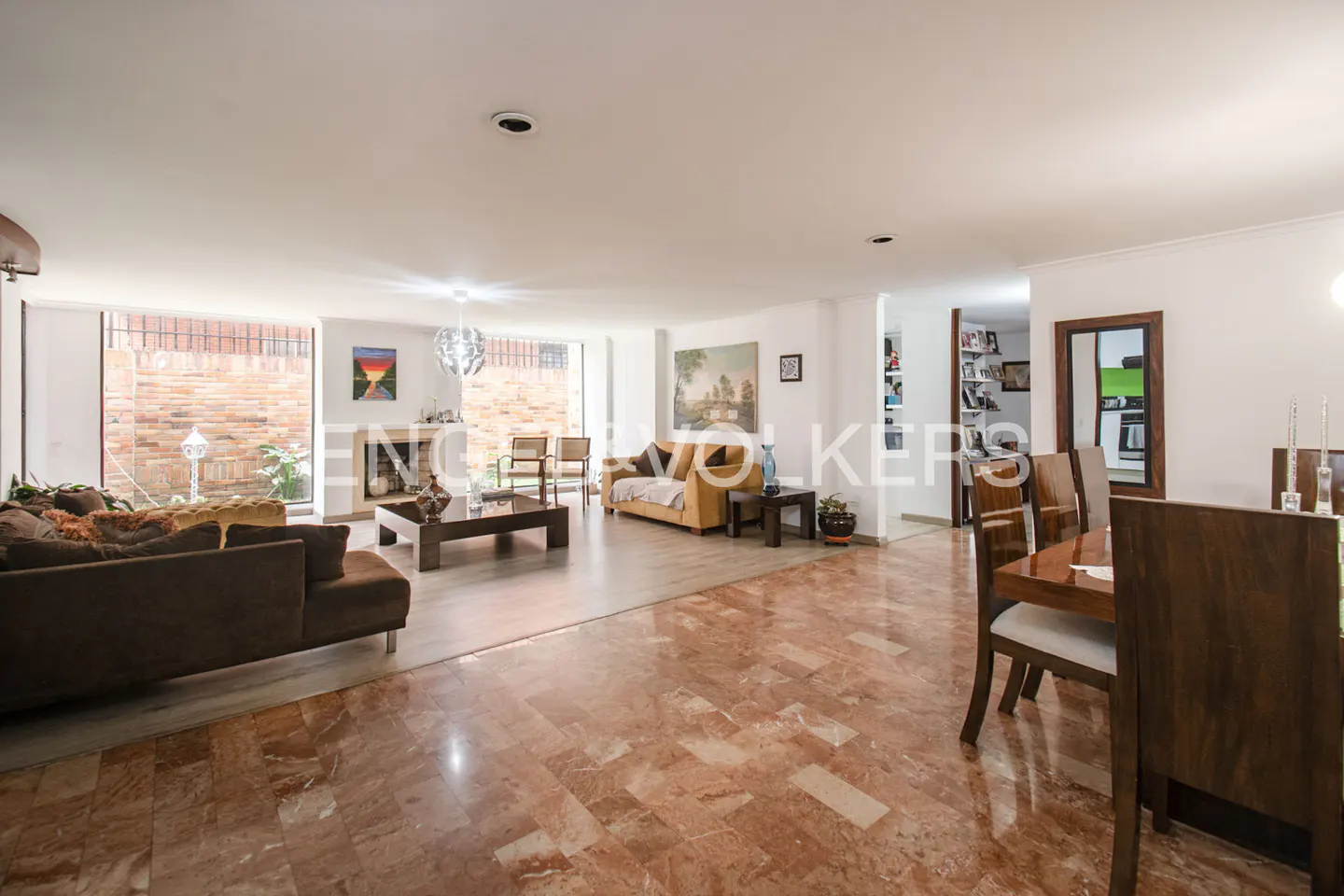 Open-concept living and dining area with brown sofas, wood table and chairs, and marble floors.