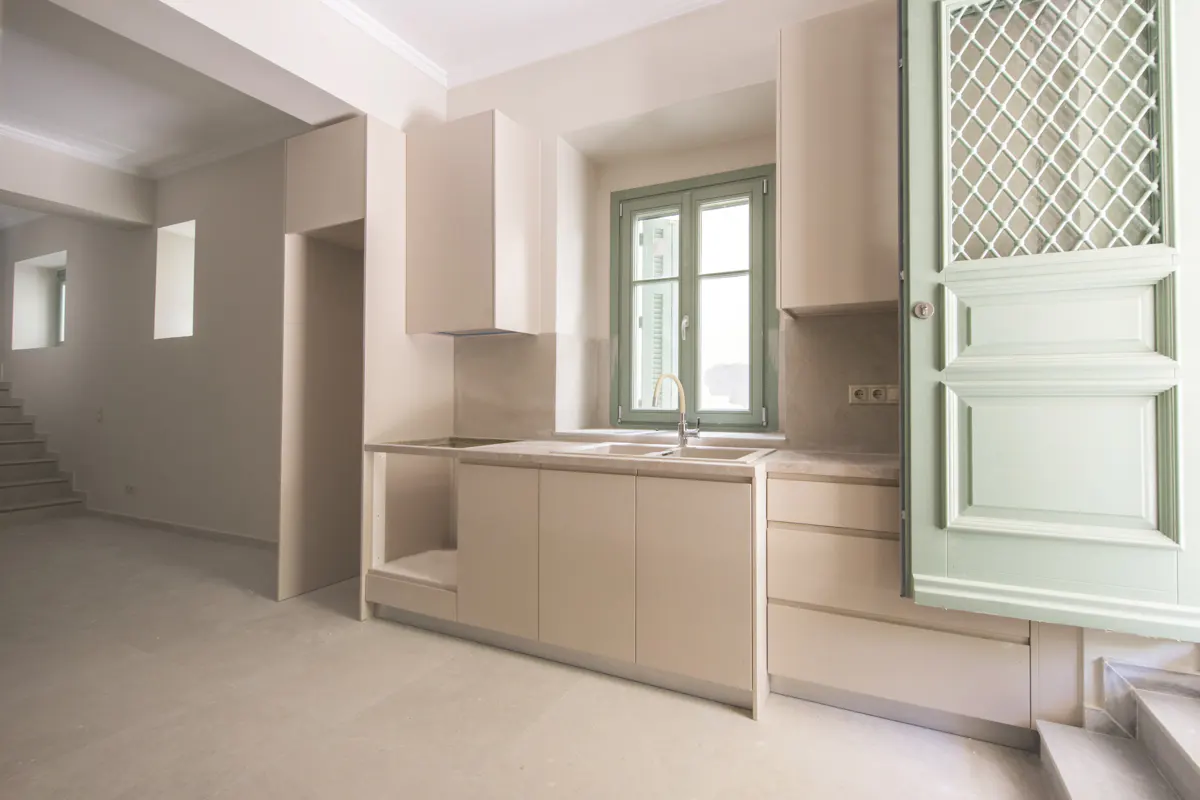 A bright, modern kitchen with beige cabinets, a green window frame, and a light green door with a white lattice design.