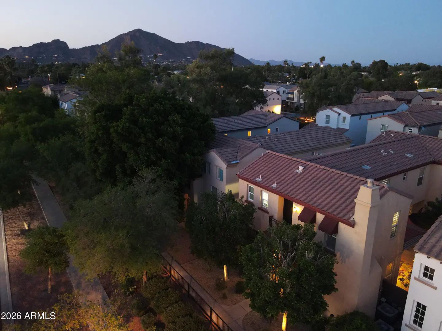 Aerial view of townhouses with red tile roofs at dusk, trees, and a mountain in the background.